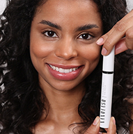 Uma mulher exibe com confiança um tubo de rímel, exibindo seu produto de beleza com um sorriso brilhante.