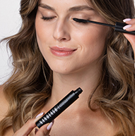 Uma mulher aplica rímel com cuidado para realçar os cílios, concentrando-se intensamente em sua rotina de maquiagem.