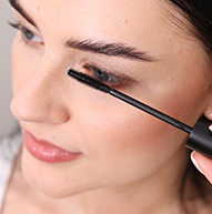 Uma mulher usa habilmente um pincel de rímel para aplicar rímel, focando nos cílios para conseguir um look definido.