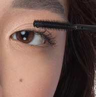 Uma mulher é vista aplicando rímel com pincel, focando nos cílios para conseguir um look definido e elegante.